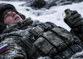 Ruský voják ležící ve sněhu s granátem